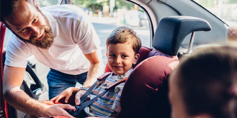 A dad strapping his child into a safety seat in the back seat of a car.